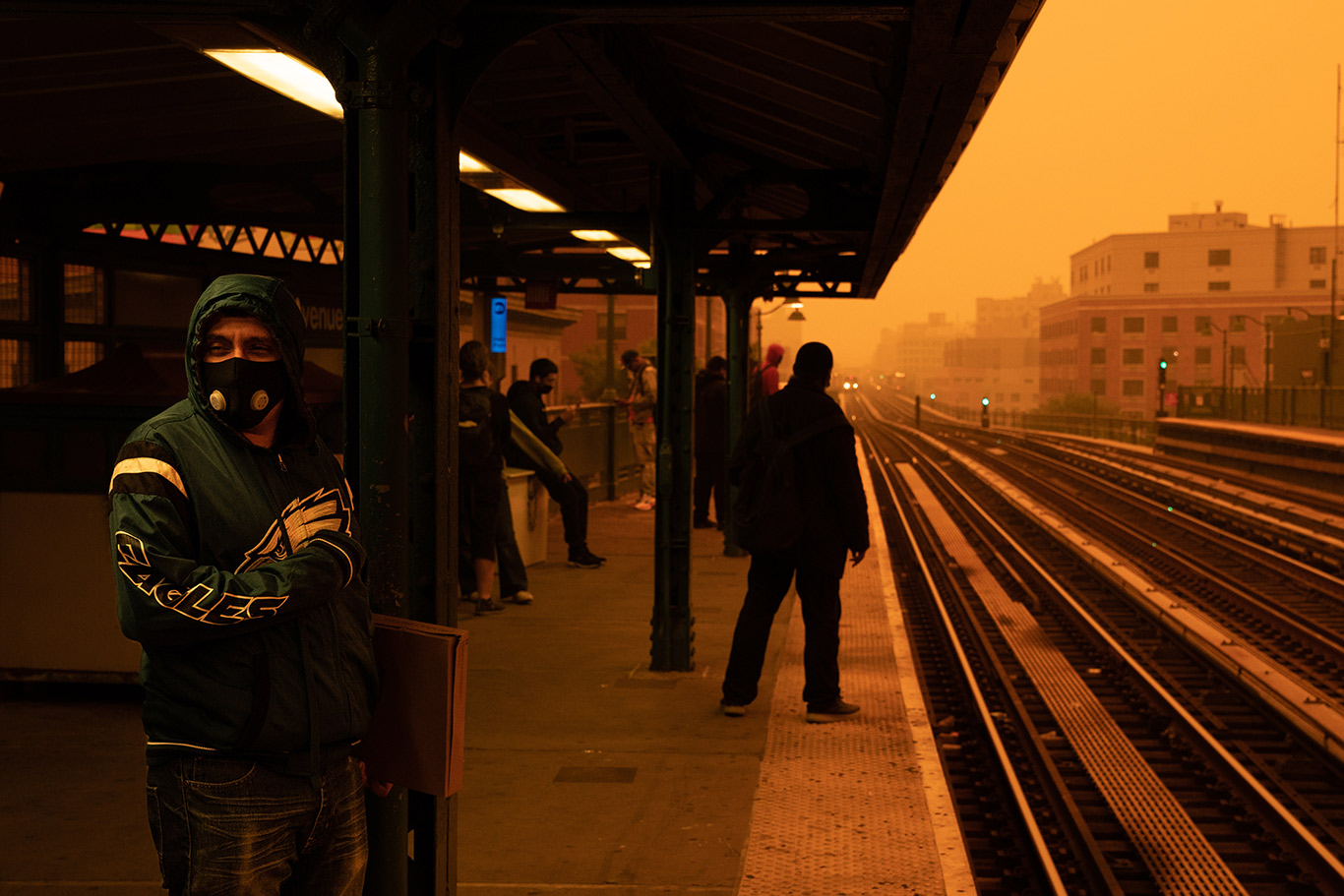 A person wearing a face mask waits for the subway in New York City with an orange, smokey sky in the background