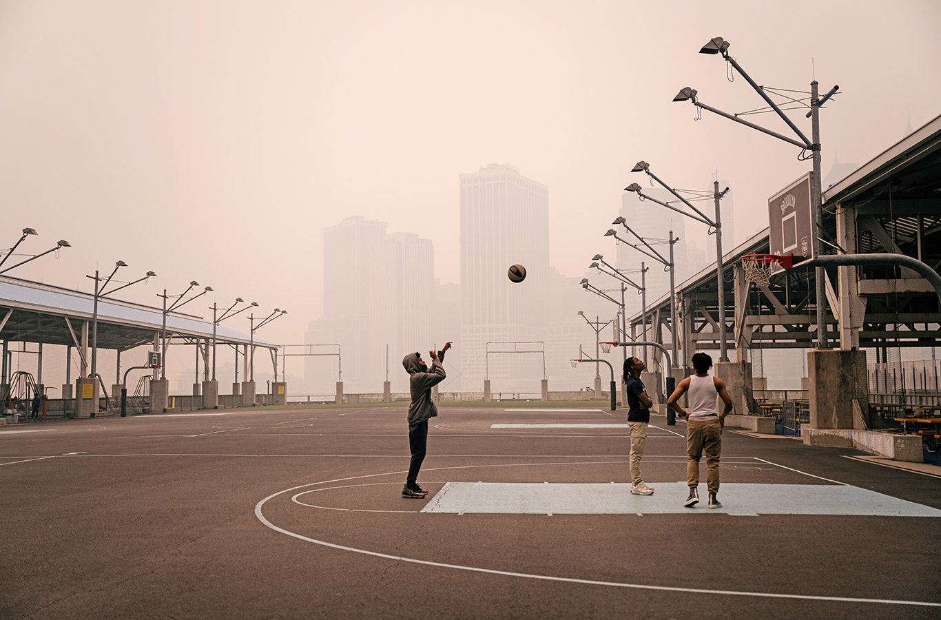 People play basketball in Brooklyn Bridge Park as the Lower Manhattan skyline is obscured by hazy skies