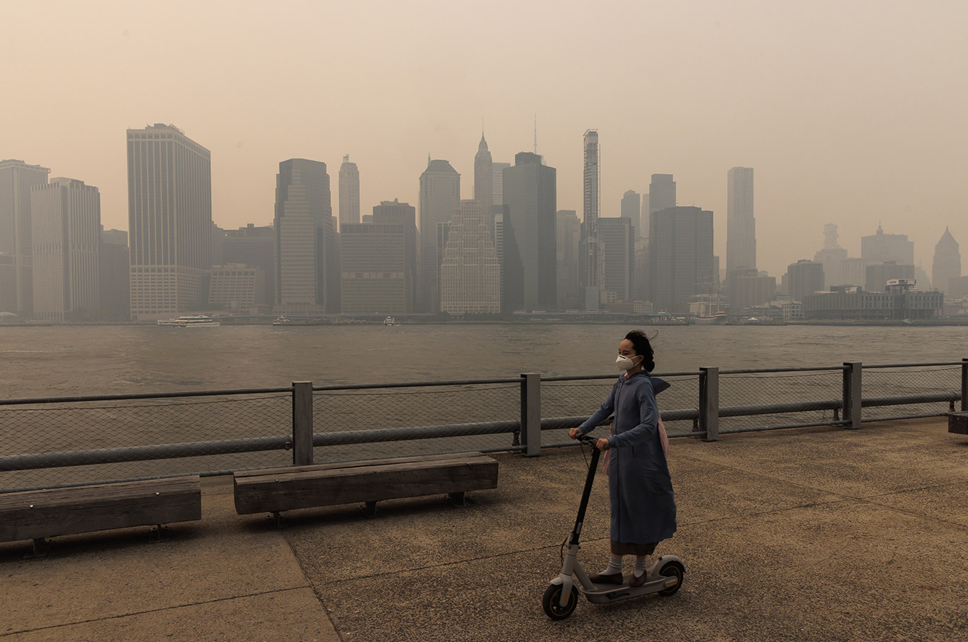 A person wearing a mask and riding scooter passes as buildings in lower Manhattan are seen through smoke filling the air 
